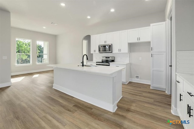 kitchen with stainless steel appliances, light hardwood / wood-style floors, a center island with sink, and sink