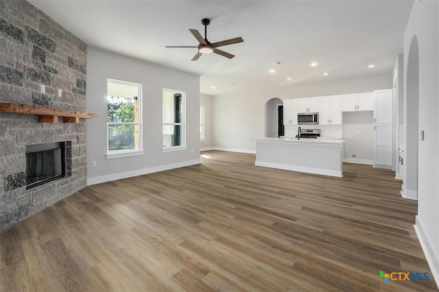 unfurnished living room with wood-type flooring, a stone fireplace, and ceiling fan