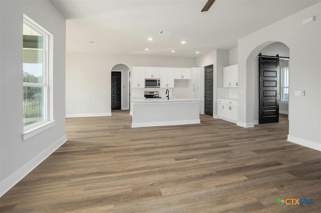 kitchen featuring white cabinets, light hardwood / wood-style flooring, a barn door, an island with sink, and stainless steel appliances