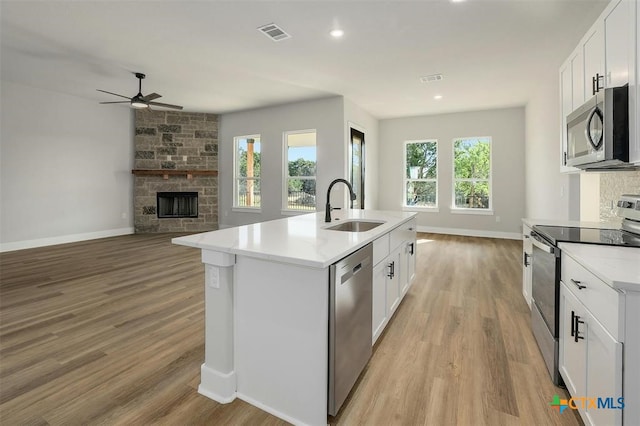 kitchen with stainless steel appliances, a kitchen island with sink, sink, a fireplace, and white cabinetry