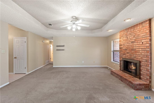 unfurnished living room with ceiling fan, carpet floors, a tray ceiling, a fireplace, and a textured ceiling