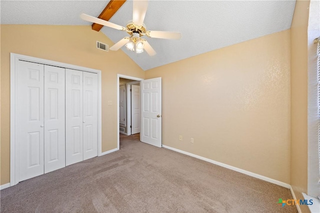 unfurnished bedroom featuring ceiling fan, light colored carpet, vaulted ceiling with beams, a textured ceiling, and a closet