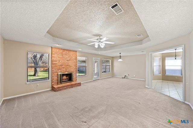 unfurnished living room with a textured ceiling, a brick fireplace, light carpet, a raised ceiling, and ceiling fan