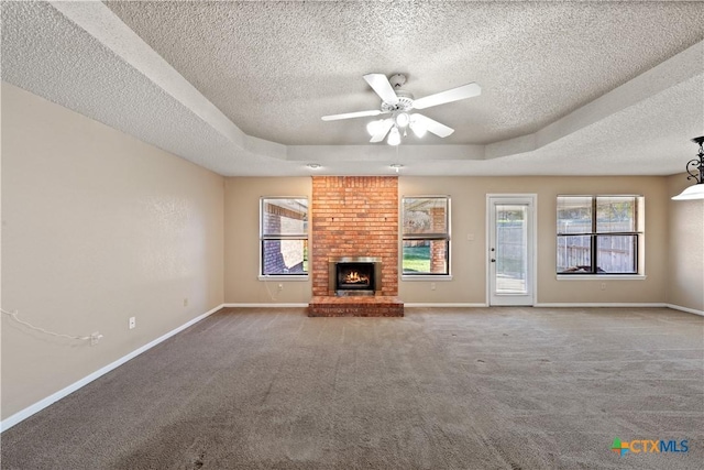 unfurnished living room with ceiling fan, carpet, a fireplace, a tray ceiling, and a textured ceiling