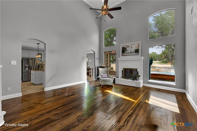 172 River Chase Dr, New Braunfels, TX 78132 - unfurnished living room featuring a towering ceiling, wood-type flooring, ceiling fan, a brick fireplace, and arched walkways