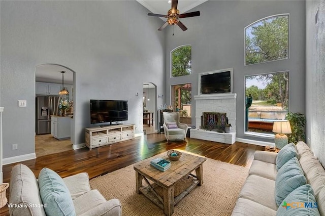 172 River Chase Dr, New Braunfels, TX 78132 - living room with arched walkways, a towering ceiling, a ceiling fan, a fireplace, and wood finished floors