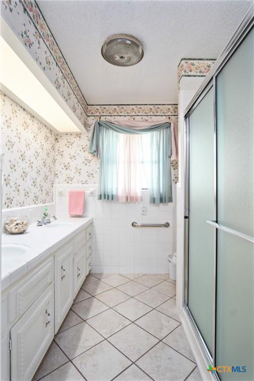 bathroom featuring a shower with shower door, vanity, tile patterned flooring, and a textured ceiling