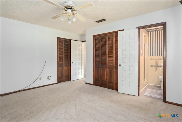 unfurnished bedroom featuring ceiling fan, light colored carpet, ensuite bathroom, and two closets