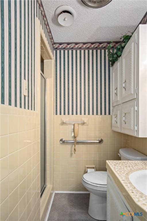 bathroom featuring toilet, a shower with door, tile walls, a textured ceiling, and vanity