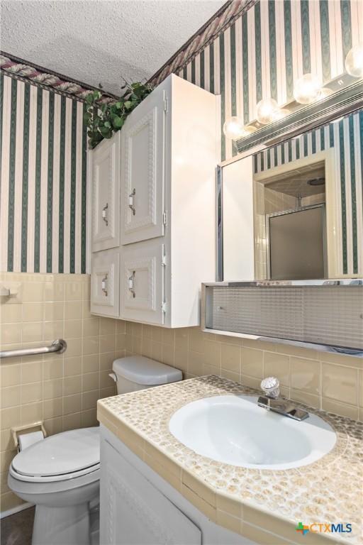 bathroom with toilet, vanity, tile walls, and a textured ceiling