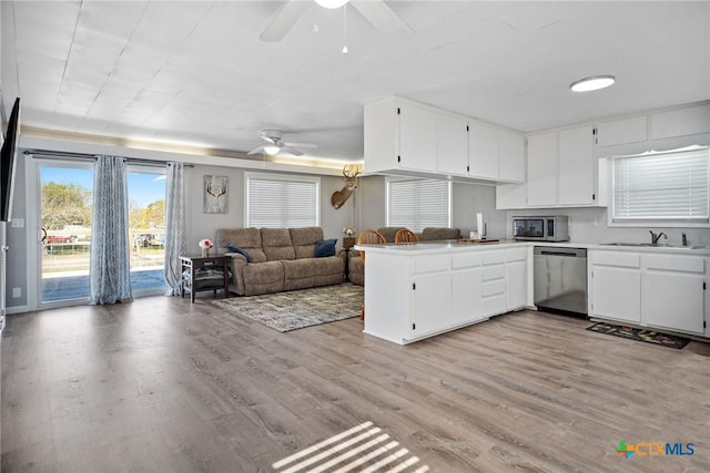 kitchen featuring open floor plan, light wood-style flooring, a peninsula, stainless steel appliances, and a sink