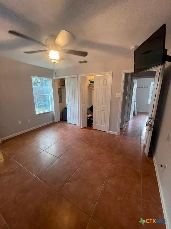 unfurnished bedroom featuring ceiling fan, dark tile patterned flooring, and a textured ceiling