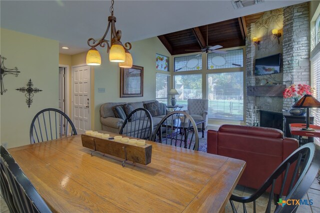 dining space featuring ceiling fan, a stone fireplace, and lofted ceiling with beams