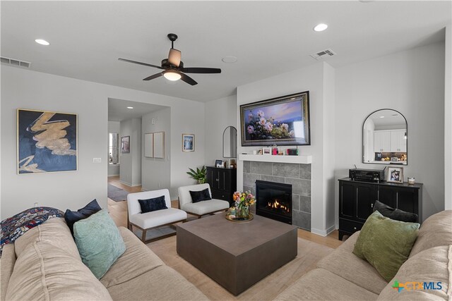 living room featuring a tiled fireplace, ceiling fan, and light hardwood / wood-style flooring