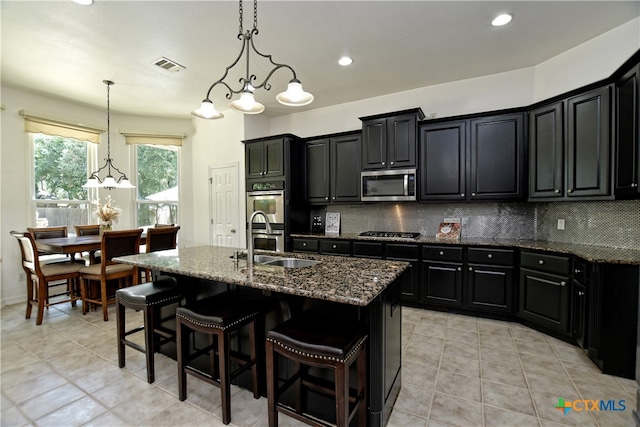 1108 Celtic Cv, Round Rock, TX 78681 - kitchen featuring stainless steel appliances, dark cabinetry, tasteful backsplash, dark stone counters, and a center island with sink