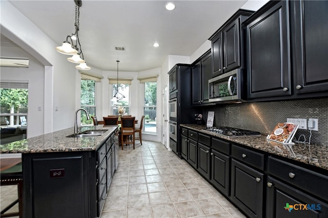 1108 Celtic Cv, Round Rock, TX 78681 - kitchen with dark cabinetry, stainless steel appliances, an island with sink, light tile patterned floors, and dark stone countertops