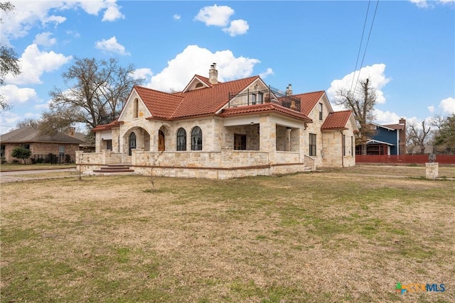 view of front of property featuring a chimney, a front lawn, a tile roof, and a balcony