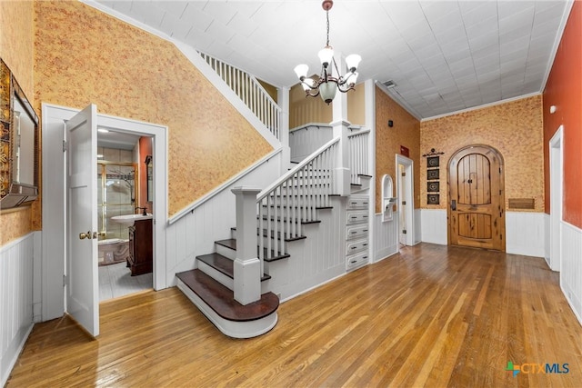 entrance foyer with wainscoting, wallpapered walls, stairs, and wood finished floors