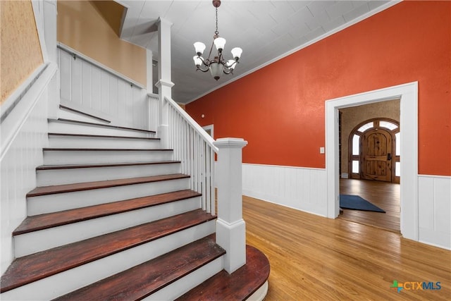 staircase featuring a wainscoted wall, wood finished floors, crown molding, and a chandelier