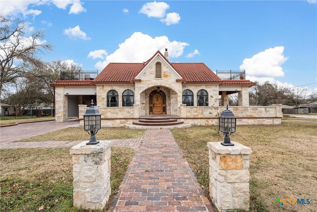 mediterranean / spanish home with a tile roof, a front yard, a chimney, a balcony, and driveway