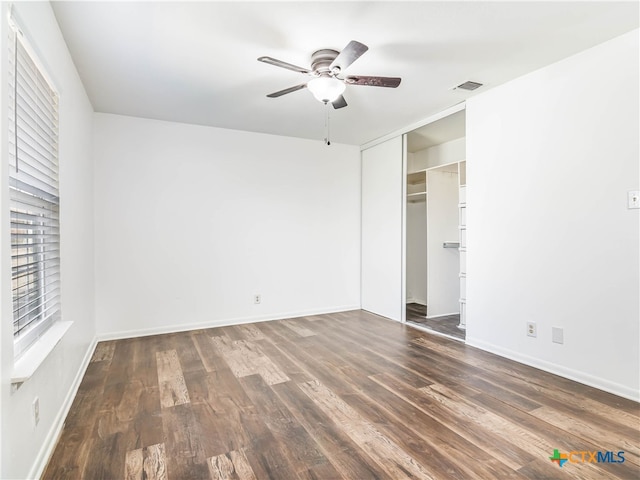 unfurnished bedroom featuring dark wood-style floors, a closet, visible vents, a ceiling fan, and baseboards