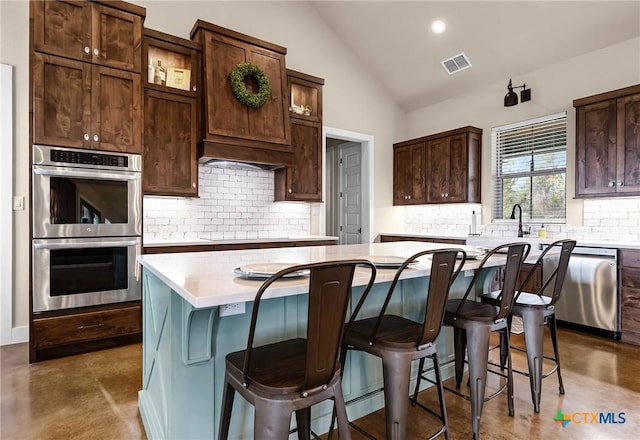 kitchen featuring backsplash, vaulted ceiling, appliances with stainless steel finishes, dark brown cabinets, and a kitchen island