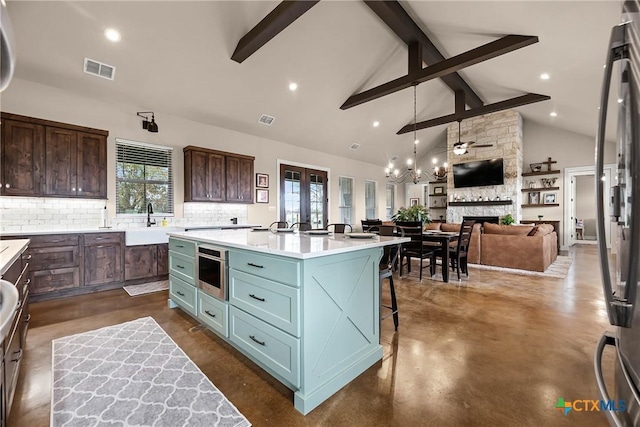 kitchen featuring decorative backsplash, stainless steel appliances, beam ceiling, a stone fireplace, and an island with sink