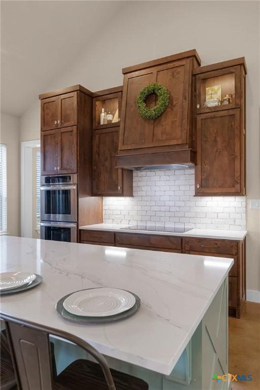 kitchen featuring lofted ceiling, premium range hood, black electric cooktop, double oven, and tasteful backsplash