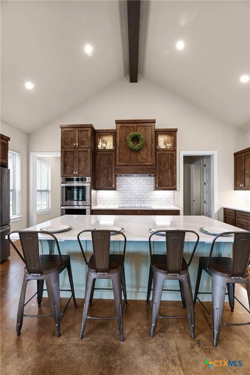 kitchen with backsplash, a kitchen breakfast bar, a spacious island, vaulted ceiling with beams, and dark brown cabinets