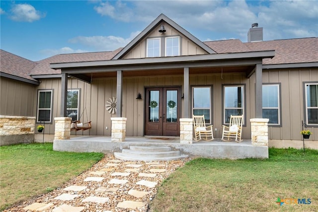 view of exterior entry featuring covered porch, french doors, and a yard