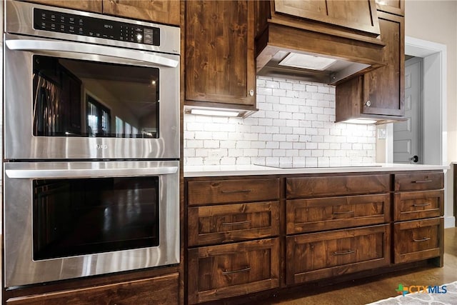 kitchen with custom exhaust hood, backsplash, black electric cooktop, double oven, and dark brown cabinetry