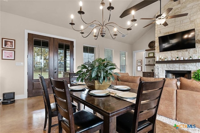 dining space featuring a stone fireplace, french doors, high vaulted ceiling, and ceiling fan with notable chandelier