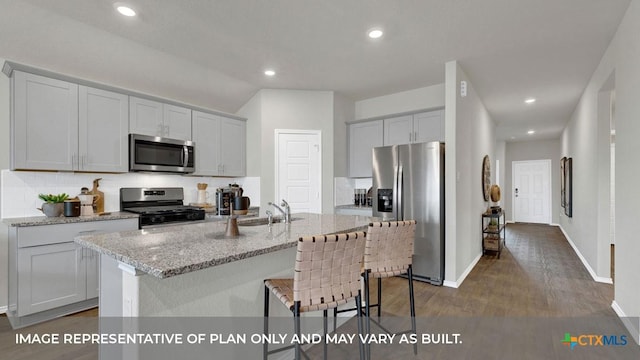 kitchen with light stone counters, dark wood-style flooring, a center island with sink, stainless steel appliances, and tasteful backsplash