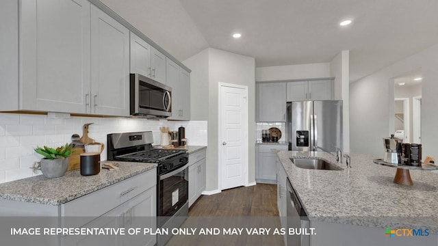 kitchen with light stone counters, appliances with stainless steel finishes, dark wood finished floors, and a sink