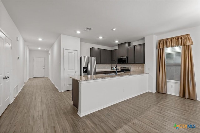 kitchen featuring tasteful backsplash, appliances with stainless steel finishes, light stone countertops, and light wood-type flooring