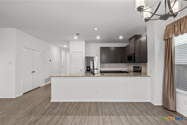 kitchen with appliances with stainless steel finishes, backsplash, hanging light fixtures, light hardwood / wood-style floors, and light stone countertops