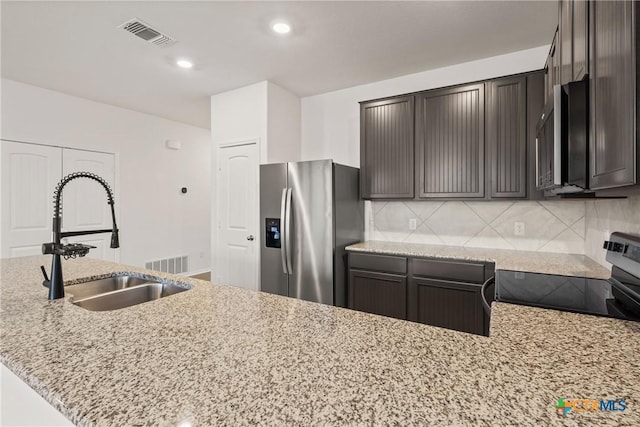 kitchen featuring light stone counters, stainless steel appliances, dark brown cabinets, and backsplash