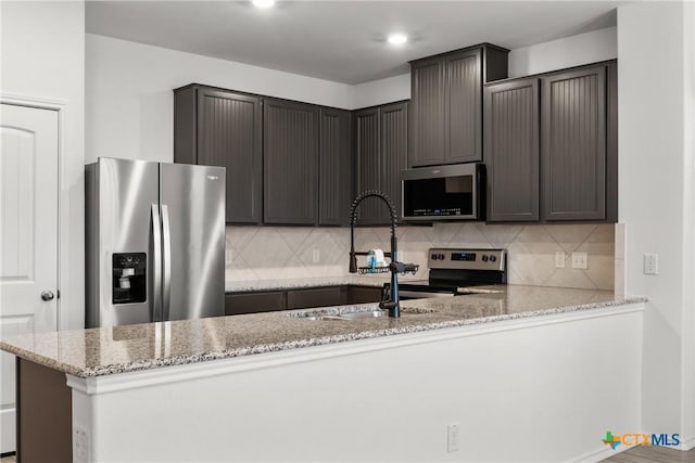 kitchen with backsplash, stainless steel appliances, light stone counters, dark brown cabinetry, and kitchen peninsula