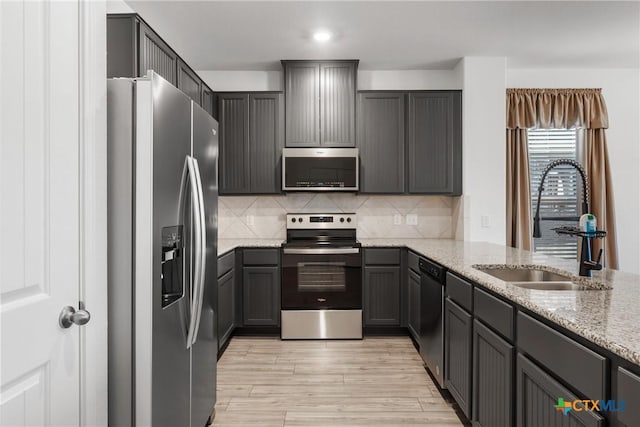 kitchen with sink, appliances with stainless steel finishes, backsplash, light stone counters, and light hardwood / wood-style floors