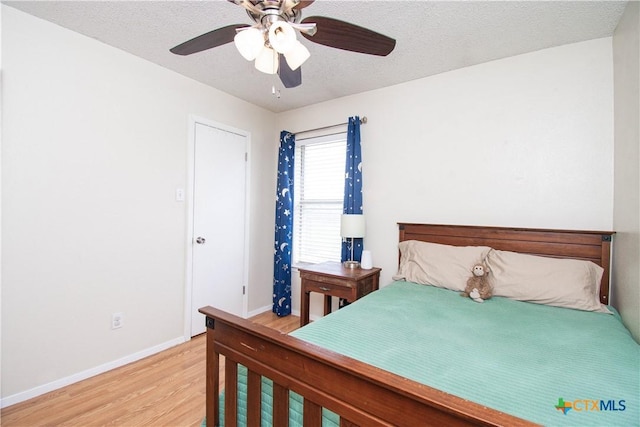 bedroom with a textured ceiling, light wood finished floors, baseboards, and a ceiling fan