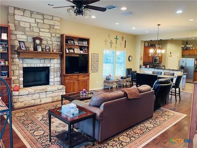 living room featuring wood-type flooring, a stone fireplace, and ceiling fan