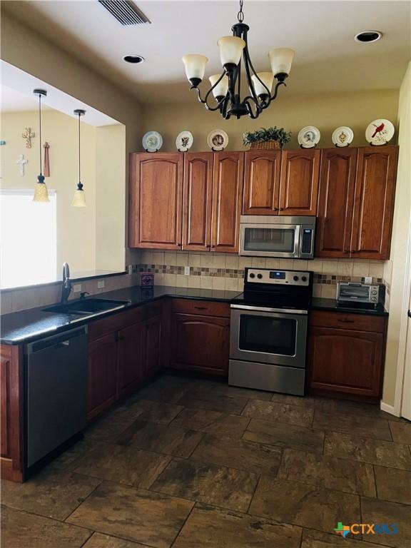 kitchen with decorative backsplash, dark countertops, stainless steel appliances, and visible vents