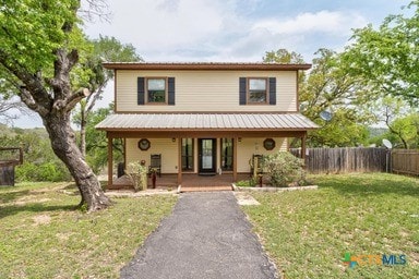 25420 Cove Dr, Spicewood, TX 78669 - traditional-style house featuring fence, covered porch, metal roof, and a front lawn