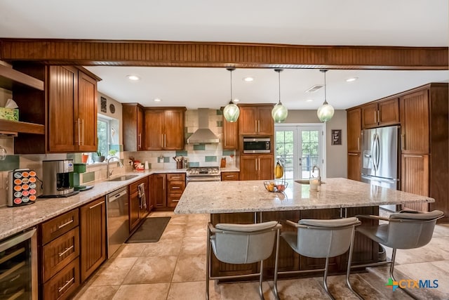 kitchen featuring a breakfast bar area, appliances with stainless steel finishes, wall chimney range hood, a sink, and wine cooler