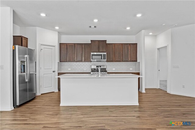 130 Carmello, Kyle, TX 78640 - kitchen with light countertops, light wood-type flooring, an island with sink, dark brown cabinetry, and appliances with stainless steel finishes