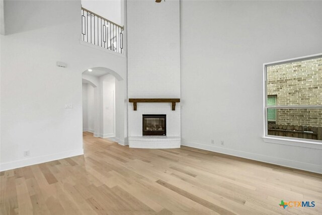 unfurnished living room with a towering ceiling, a large fireplace, arched walkways, wood finished floors, and baseboards