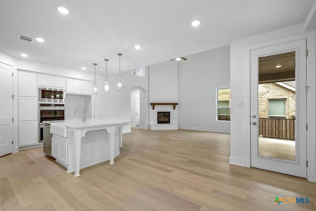 kitchen with white cabinets, light wood finished floors, light countertops, a glass covered fireplace, and stainless steel appliances