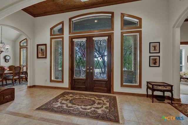 tiled entryway featuring an inviting chandelier, wood ceiling, ornamental molding, and french doors