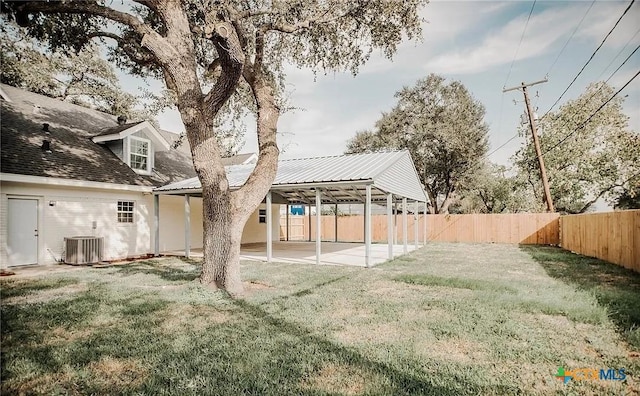 rear view of property featuring a carport, central AC unit, a lawn, and a fenced backyard