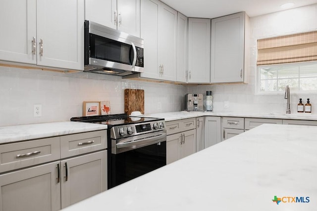 kitchen with appliances with stainless steel finishes, backsplash, light stone countertops, gray cabinets, and a sink